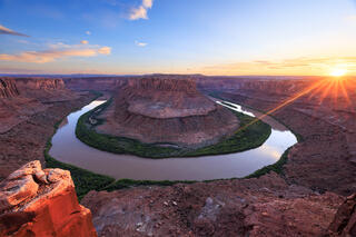 A huge bend in the green river. The view is looking down into a huge desert canyon. The sun is setting and is seen on the far side of the image.