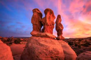 Three Hoodoos bathed in warm redish orange glow of light cast from a colorful sunset.