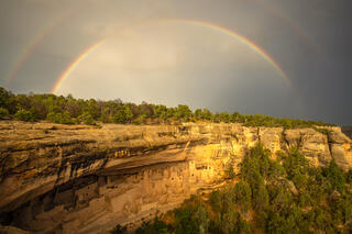 The cliff palace of mese verde with a double rainbow above it on a stormy day.