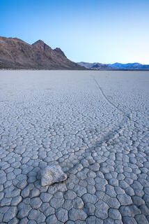 A rock found on a desert playa with a mud track race line leading away in the distance. 