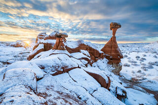 The main hoodoo of the Toadstools trail covered in snow while the sun peaks through the clouds lighting the landscape. 