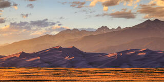 Light bleeds across the landscape at sunset. The star dunes and the rocky mountains are seen in the background.