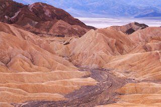 A dark river channel cuts through warm yellow hills. A white salt playa can be seen in the distance. 