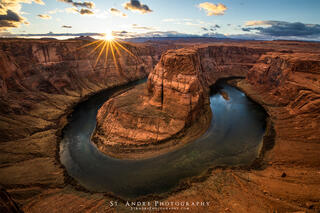 Horseshoe bend at sunset with a large sun star at the top of the image and the colorado river flowing through the canyon. 