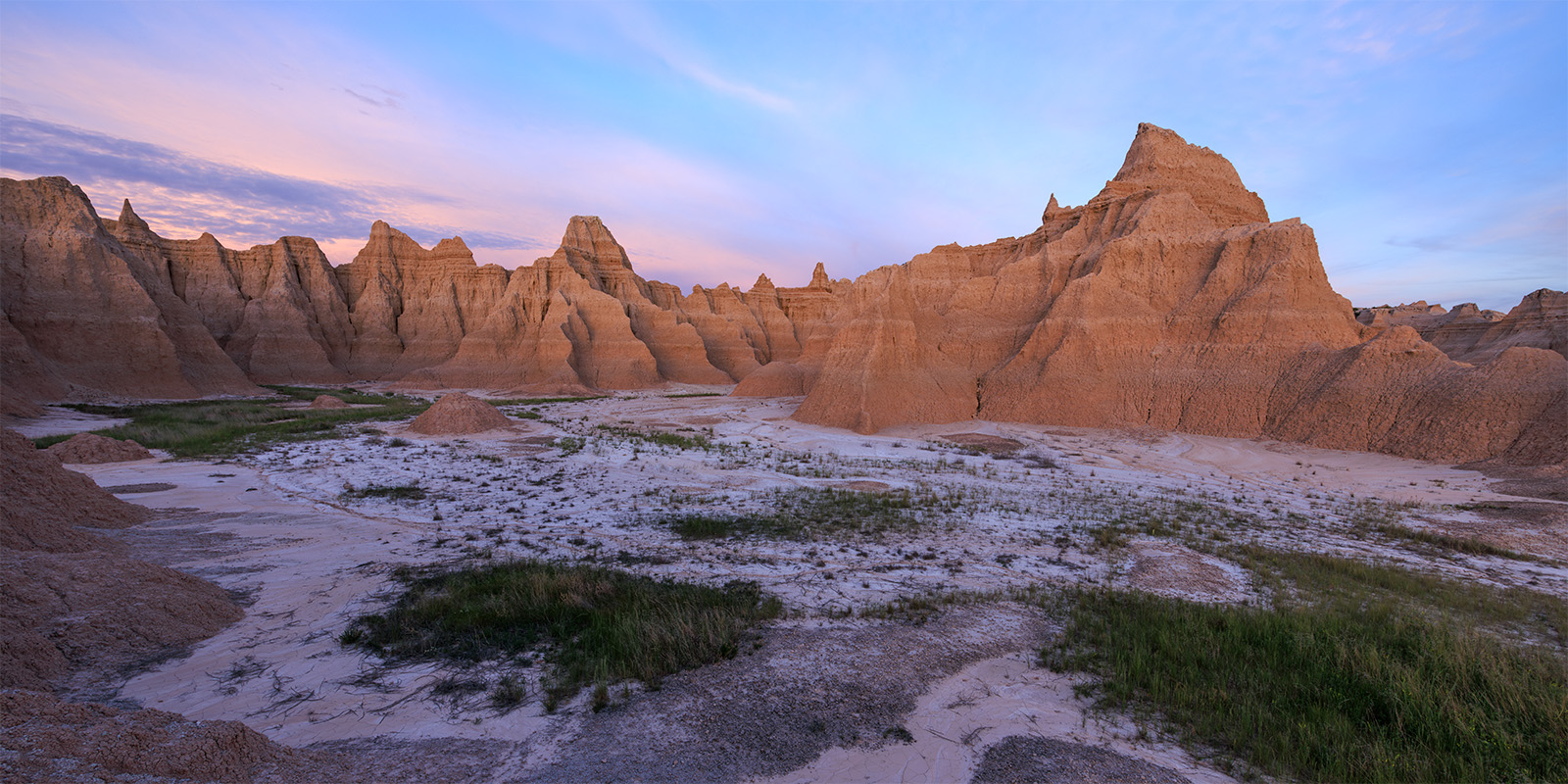 A Bug Planet A series of spires lit by the setting sun. Soft pastel colors exist within the sky while grass spreads into the muddy earth.