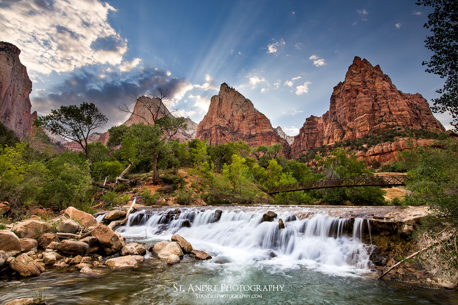 Rays of light shine over the Court of the Patriarchs in Zion National Park. Along with this a small waterfall cascades down over rocks. 