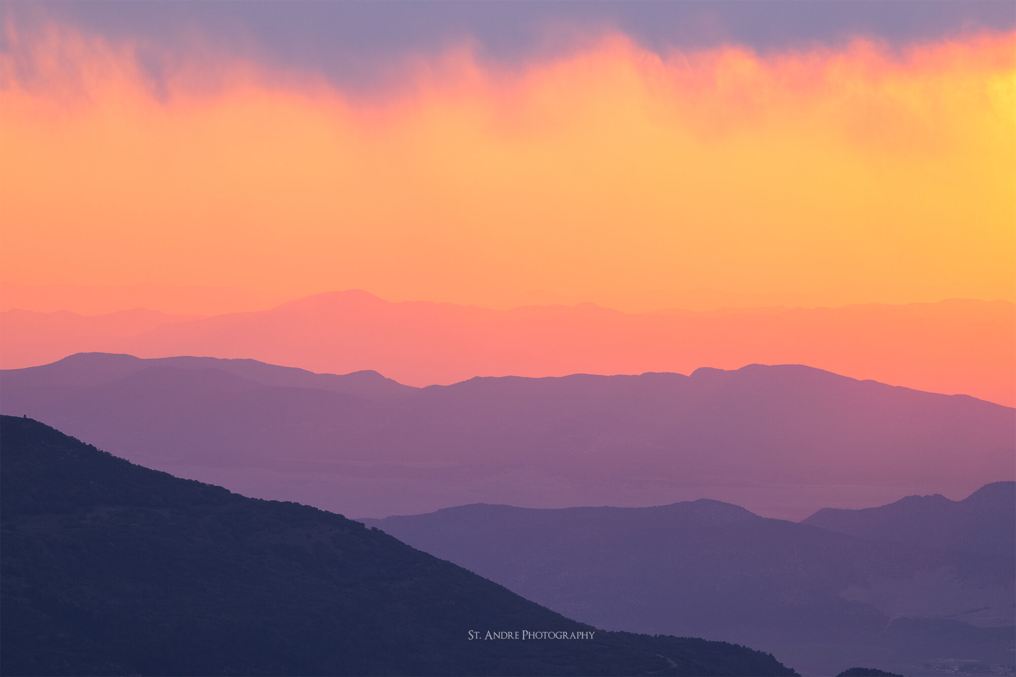 Mountain ranges disappearing into the distance. The overall color tone of the image is red due to smoke in the atmosphere. 