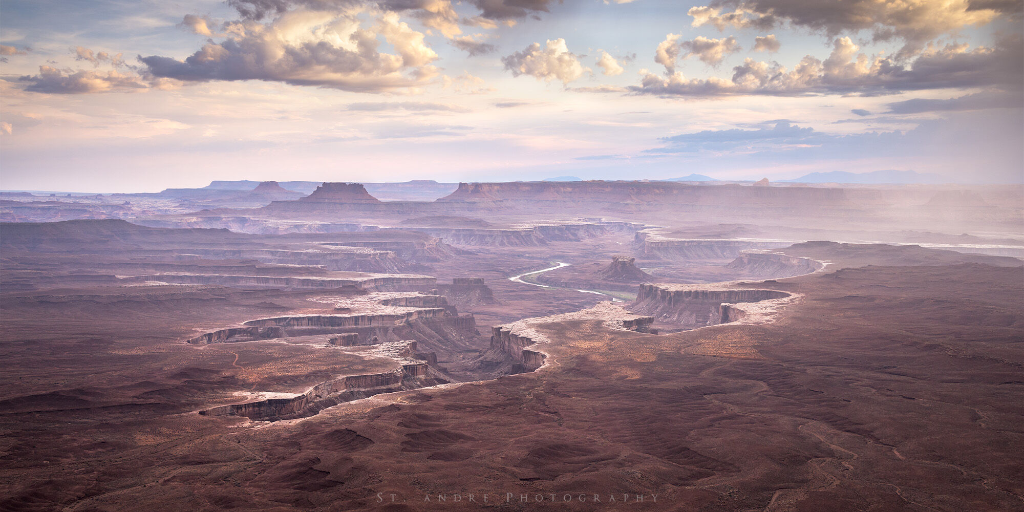 Green river overlook. A large canyon expands below the viewer with a large river cutting through the desert. A thunderstorm is raining in the image. 