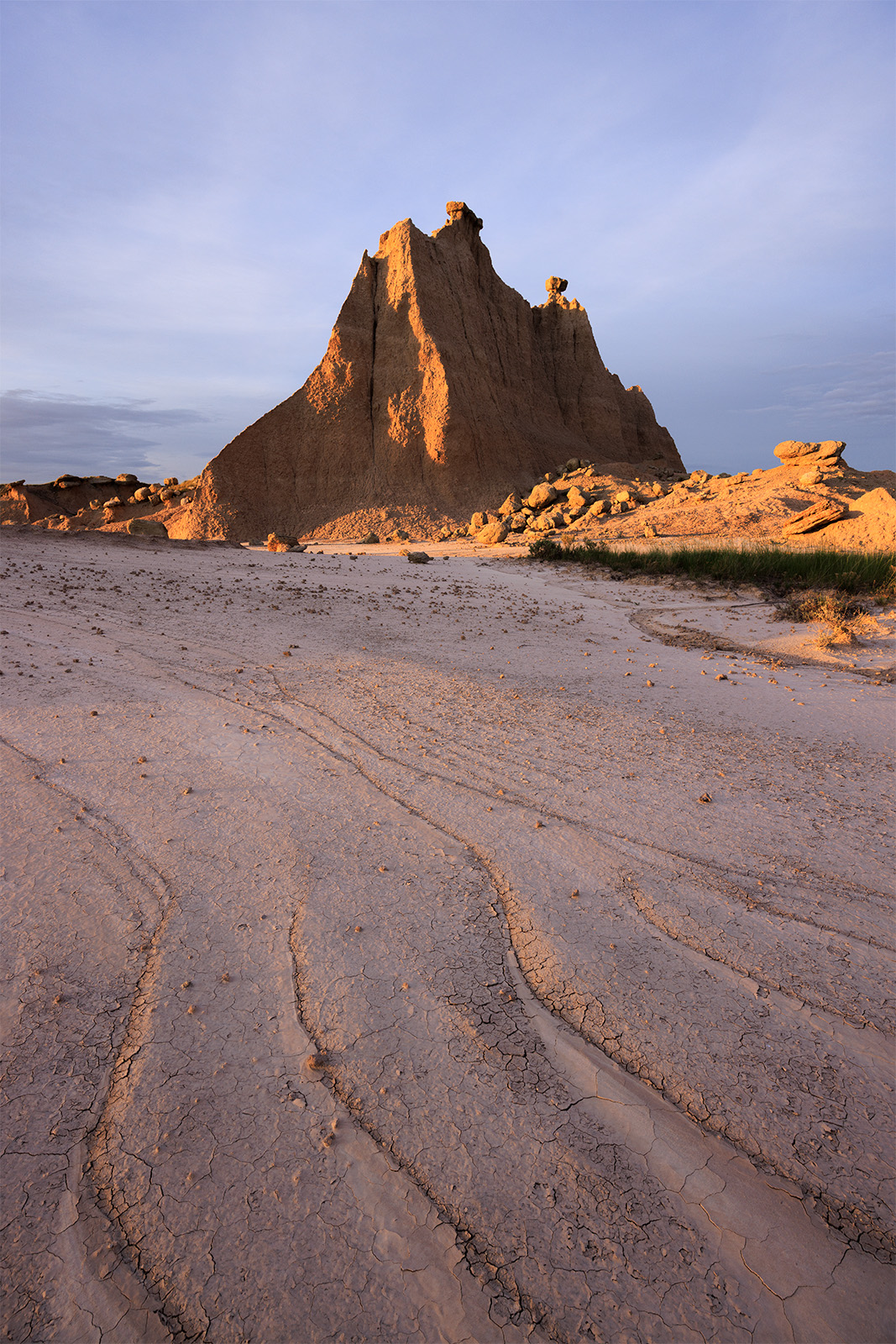 Hoodoo Fins A large tower with little hoodoos on top of in badlands. The front of the image includes a few swirls of mud lit by the setting sun.