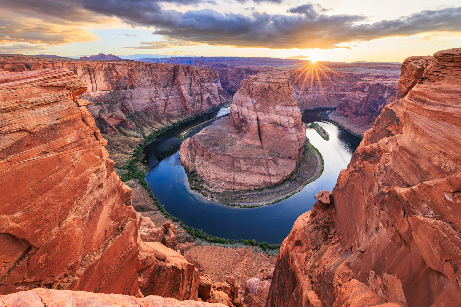 An image of Horseshoe Bend in Arizona. The Colorado River deep in the bottom of the canyon wraps around a large bend. A beautiful sunset is going on.