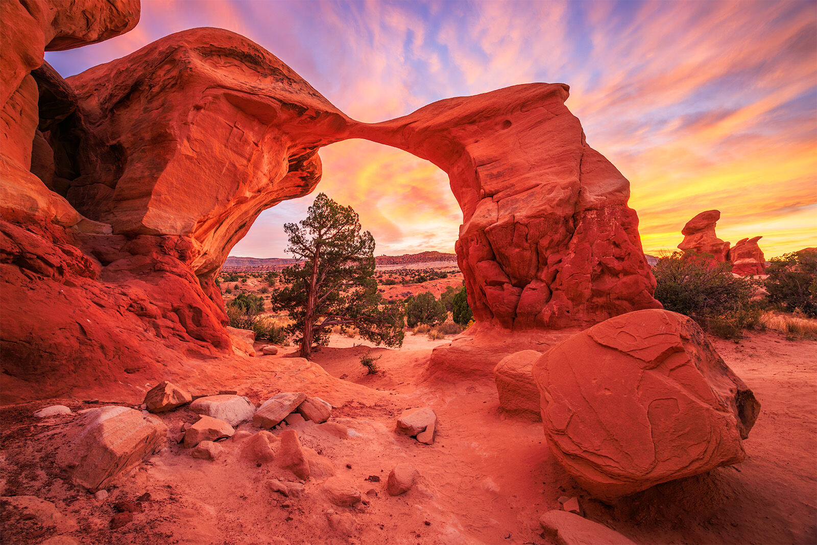 Metate Arch, a small arch in the desert of southern Utah. The image is bathed in colorful light from a colorful sunset. 
