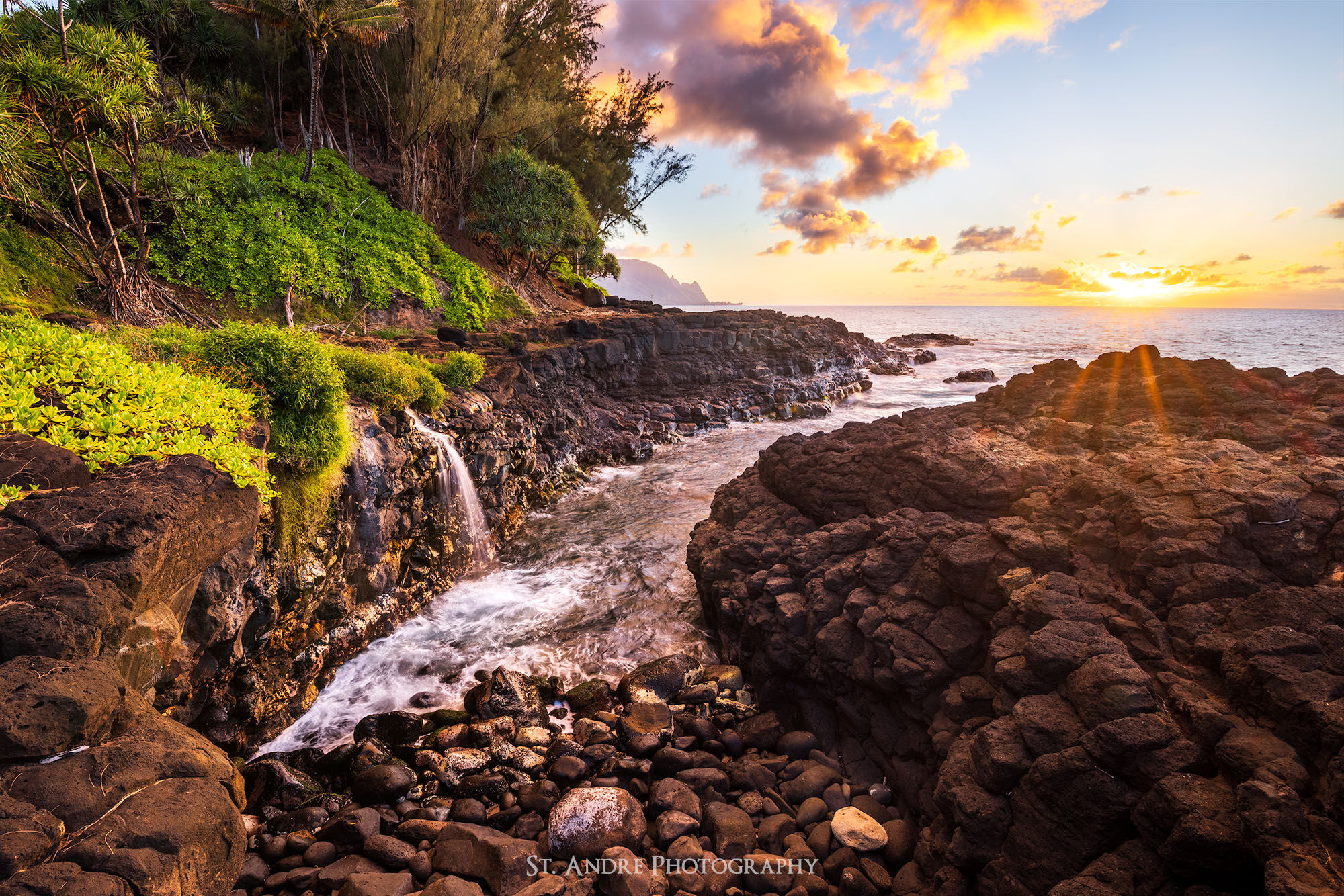 A small stream cascades off lava rock into a small alcove where the ocean cascades up onto black volcanic rock. 