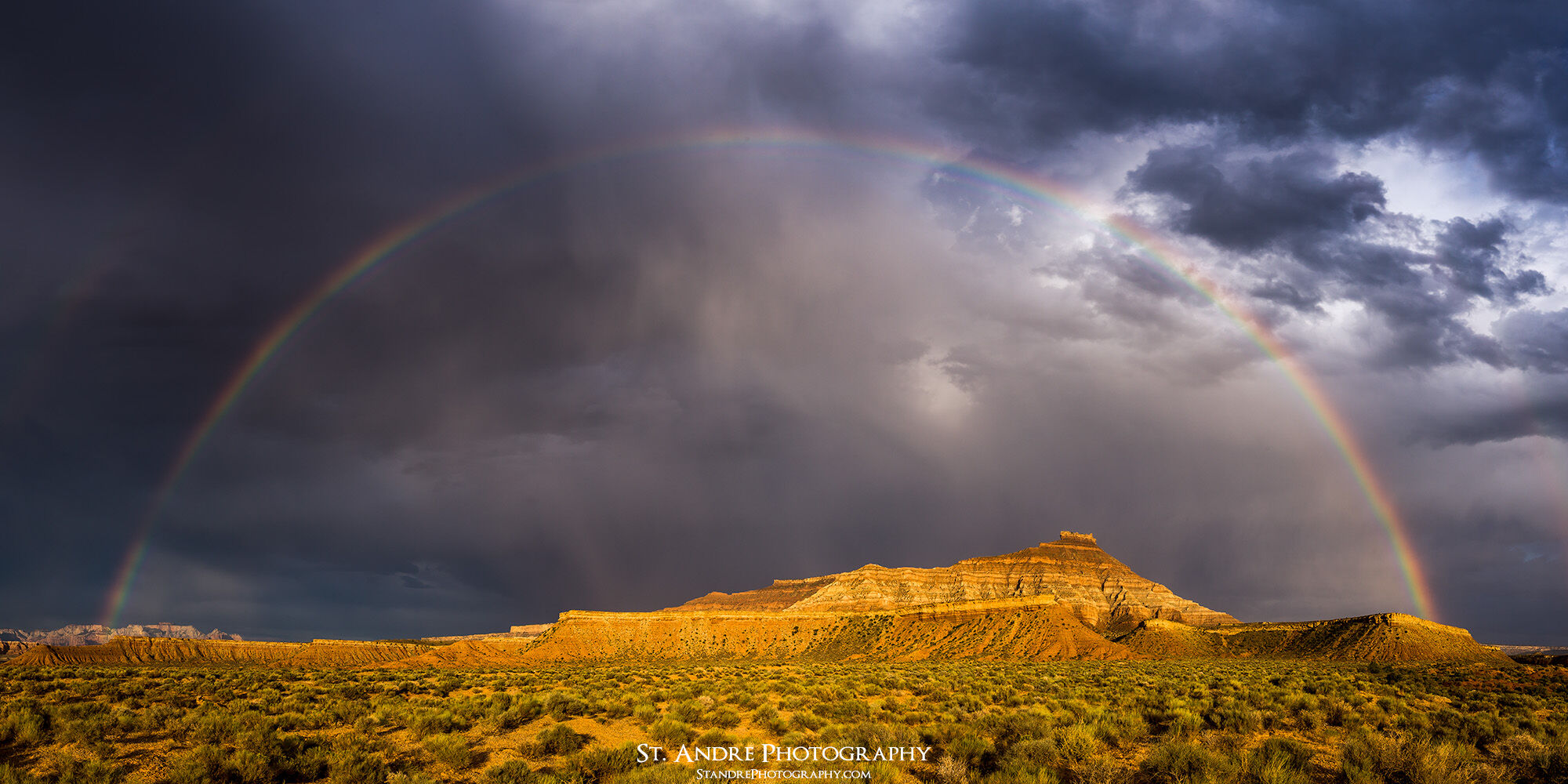 A large rainbow arches over Gooseberry mesa with the left side landing on the west temple of Zion and the right side resting on Gooseberry Mesa.