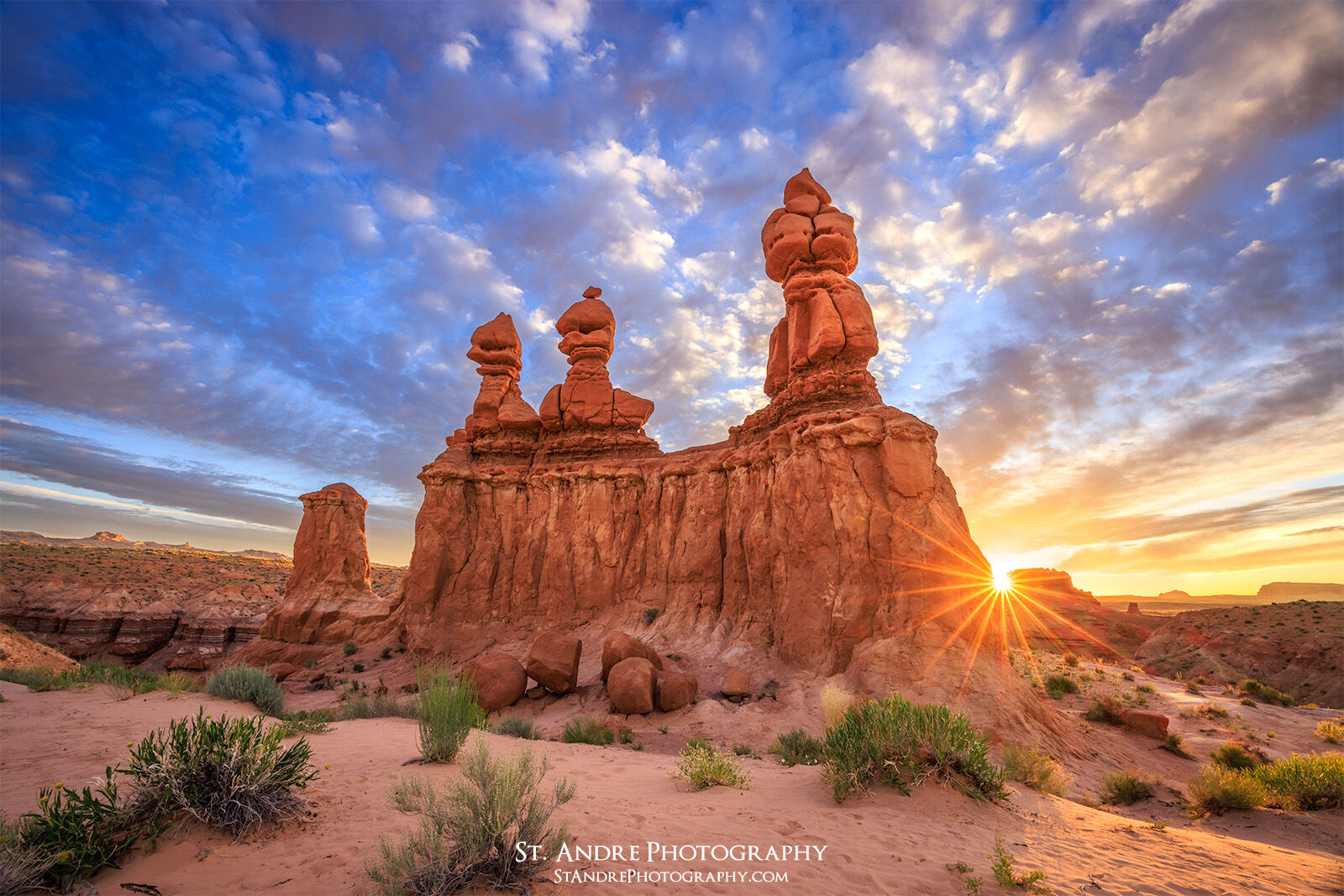 The three sisters hoodoos in goblin valley backlit by the rising sun with a small sun star in the bottom corner of the image. 