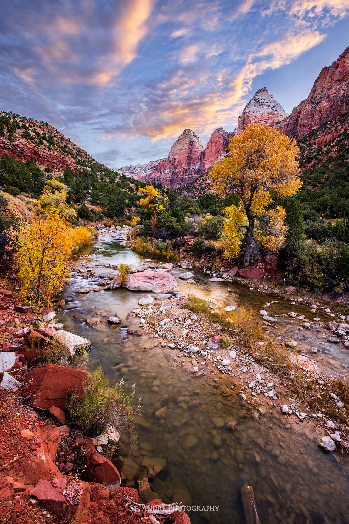 Temple of the sun mountain and the two brothers peaks are viewed with the virgin river cutting through a canyon and cottonwood trees in full fall colors. 