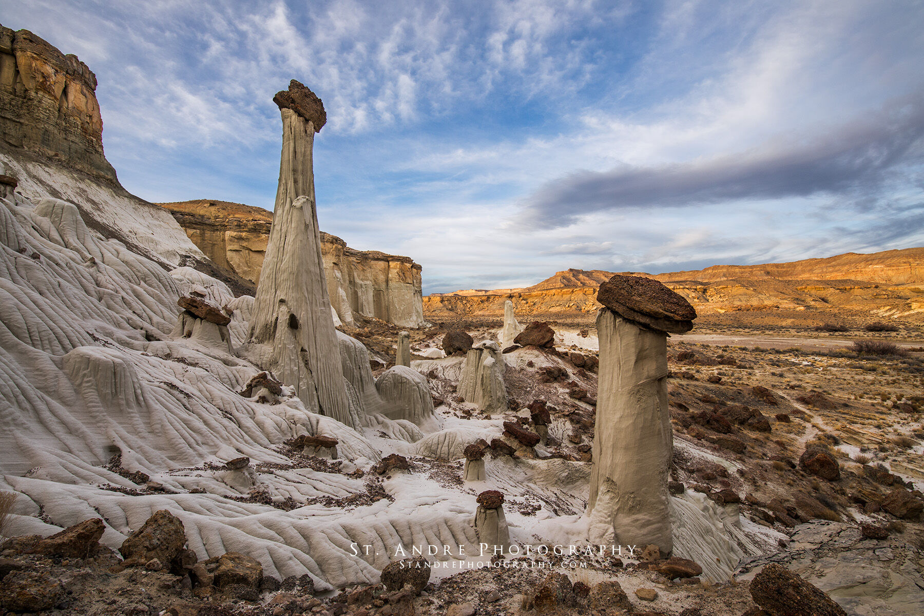 Wahweap Hoodoos. Two large hoodoos stand on the edge of a cliff with soft passing clouds. 