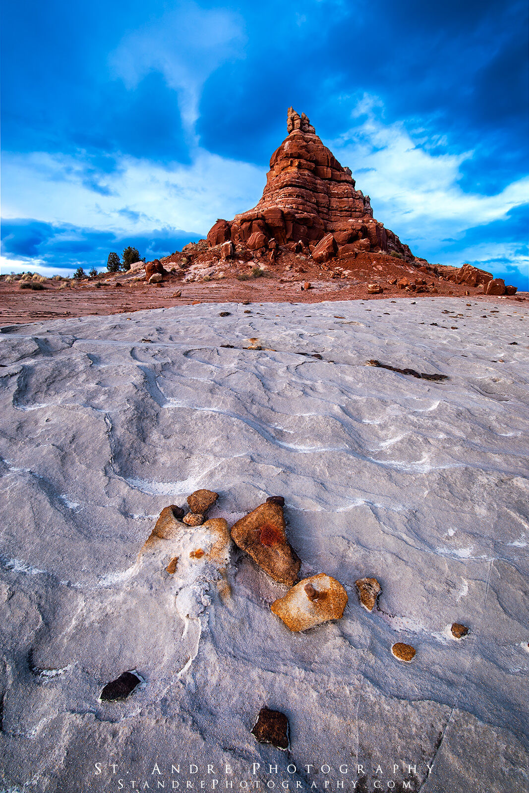 A large sandstone tower with a collection of rocks around its base. Storm clouds hang in the skies above.